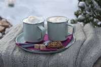 Cups with a hot cappuccino on plates with sugar, biscuits, and teaspoons