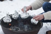 A woman placing potatoes in aluminum foil on the grill