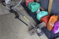 A professional Stihl strimmer lies on the floor in front of a row of fuel containers. Derryn Bank. Autumn.