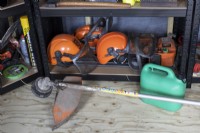 A professional Stihl strimmer lies on the floor in front of safety equipment and other paraphanalia including hard hats and visors.  Autumn.