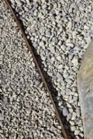 Rusted metal strip used as dividing detail on gravel pathway.