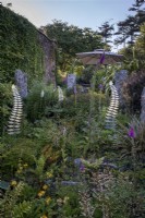 Deep cottage style garden borders studded with Granite standing stones and Galvanised steel fern by Cornish artisan 'Steeling nature'