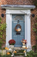 Front door and stone steps decorated for Halloween with container of Chrysanthemums, squashes, Dahlias, candles and willow wreath