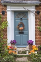 Front door and stone steps decorated for Halloween with pots of Asters, squashes, candles and willow wreath with Dahlias