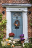 Front door and stone steps decorated for Halloween with pots of Asters and Chrysanthemums, squashes, candles and willow wreath with Dahlias