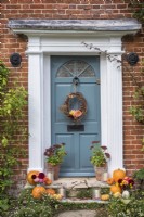 Front door with wreath and stone steps decorated for Halloween with pots of Sedums, squashes, flowers and candles 
