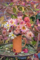 Bouquet of peach and orange Dahlias and Chrysanthemums in orange pottery vase on rusty metal chair