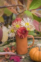Small orange pottery vase with peach and orange Dahlias and Chrysanthemums displayed on rusty metal chair