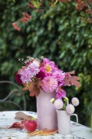 Bouquet of pink, red and lilac Dahlias and Chrysanthemums and autumn leaves in pink pottery vases on metal table