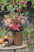 Autumn bouquet of flowers arranged in pottery vase on rusty chair in orchard - Dahlias, Asters, Sedum, blackberries and Hawthorn