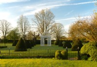 A white iron gazebo surrounded by pyramids of Taxus baccata on the Parterre Lawn at Chenies Manor.