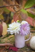 Small lilac pottery vase with purple and white Dahlias and Chyrsanthemums displayed on rusty metal chair
