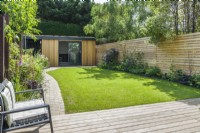 Garden office at the end of a contemporary garden with lawn, stone block path and slatted timber fencing. June