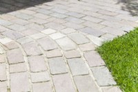 Detail of path and paving made with natural stone blocks set in cement next to lawn. June