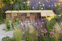 Insect hotel built into a wood and gabion bench surrounded by planting of Salvia 'Purple Rain', Gaura, Stipa tenuissima and Achillea 'Credo' - Turfed Out Garden, RHS Hampton Court Palace Garden Festival 2022