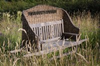 Wooden bench with a woven willow cover in the wild flower meadow at Cow Close Cottage, North Yorkshire in July full of knapweed and meadowsweet
