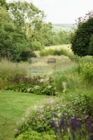 Borders at Cow Close Cottage, North Yorkshire in July planted with pinks and purples with wildflower meadow beyond.