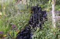 Black charred posts surrounded by planting of Persicaria amplexicaulis 'Alba' - The Yeo Valley Organic Garden, RHS Chelsea Flower Show 2021