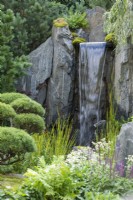 Waterfall cascading over rocks surrounded by pines - Bodmin Jail: 60 Degrees East - A Garden between Continents, RHS Chelsea Flower Show 2021