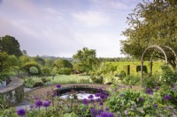 Formal terraced rose garden with circular pond and lots of Allium 'Purple Sensation' in May.