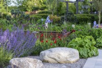 Large boulders are set into stone chippings beside a border planted with catmint, geum and allium.
