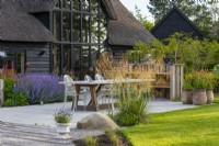 A dining terrace is edged in pots of orange geum, a clump of golden oats, Stipa gigantea, catmint and lupins.