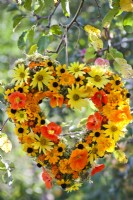 Summer wreath made of rudbeckia, nasturtium, sunflowers, pot and signet marigold hanging from the tree.