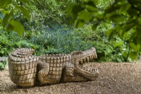 Large carved wooden Reptile sculpture set on bark chippings in a woodland garden children's play area. Cambridge Botanic Gardens. May.