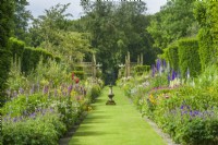 View of double herbaceous borders and gothic timber trellis. June. Grass paths and sundial at intersection.
