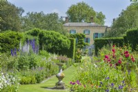 View of double herbaceous borders and Abbots Ripton Hall, June. Grass paths and sundial
.