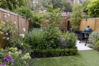 Secluded suburban garden with artificial lawn, herbaceous border and contemporary wood boundary fence.