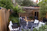 Small suburban garden with lighting at dusk with man and woman eating food in seating area