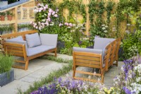 Seating area set surrounded by pastel planting with pink roses - Knolling with Daisies, RHS Hampton Court Palace Garden Festival 2022