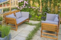 Seating area set surrounded by storage wall and pastel planting including  Erigeron 'Sea Breezes' and pink roses in Knolling with Daisies, RHS Hampton Court Palace Garden Festival 2022

