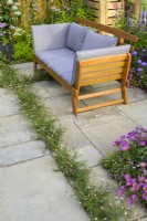 Seating area set surrounded by  planting including  Erigeron 'Sea Breezes' along paving slabs -  #knollingwithdaisies garden at RHS Hampton Court Palace Garden Festival 2022
