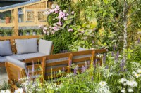 Outdoor shelving and seating area surrounded by pastel planting with white Cosmos and pink roses in #knollingwithdaisies garden at RHS Hampton Court Palace Garden Festival 2022