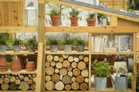 Wooden modular wall storage and display  made from reclaimed timber with logs and Erigeron karvinskianus 'Profusion' - Mexican fleabane in containers in #knollingwithdaisies garden at RHS Hampton Court Palace Garden Festival 2022
