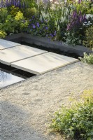Stepping-stone bridge over rill water feature with perennial planting in The Joy Club Garden at RHS Hampton Court Palace Garden Festival 2022k