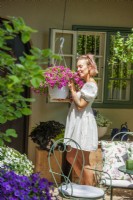 Young woman with Calibrachoa in hanging basket, summer July