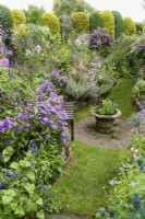 Sunken area of a cottage garden with colour themed borders and an urn of purple verbenas in July