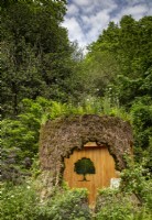 A woodland wildlife friendly garden with an oak tree trunk shelter with a living planted roof on the Connected by EXANTE Garden - RHS Chelsea Flower Show 2022 - Designed by Designer Taina Suonio - Built by Nicholsons 
