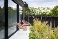 Seating area with pink chairs and table between large sliding glass doors and border with Calamagrostis brachytricha