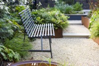 Black metal bench placed on gravel path with steps and raised corten beds. 