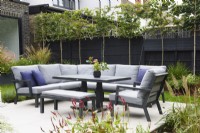 Seating area surrounded by raised flower beds and pleached trees. 