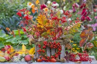 Outdoor arrangement with mixed autumn foliage, guelder rose berries and wreath made of moss and rose hips.