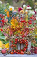 Outdoor arrangement with mixed autumn foliage, guelder rose and wreath made of moss and rosehips.