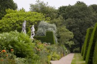 Stone statues, herbaceous borders and Taxus baccata topiary along a gravel path at Renishaw Hall and Gardens.