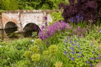 Main bridge with heron sculpture in the centre to deter the real thing (it doesn't work). Foreground planting includes Euphorbia characias subsp. wulfenii, Geranium x magnificum, larkspur, and Tellima grandiflora. Also Iris sibirica and Cotinus coggrygia in the background.