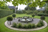 Circular gravel bed with pond and fountain and bordered by lollipop topiary at The Burrows Gardens, Derbyshire, in August
