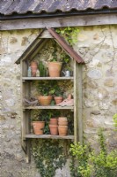 Wooden shelves with a display of terracotta pots and found objects on a stone wall